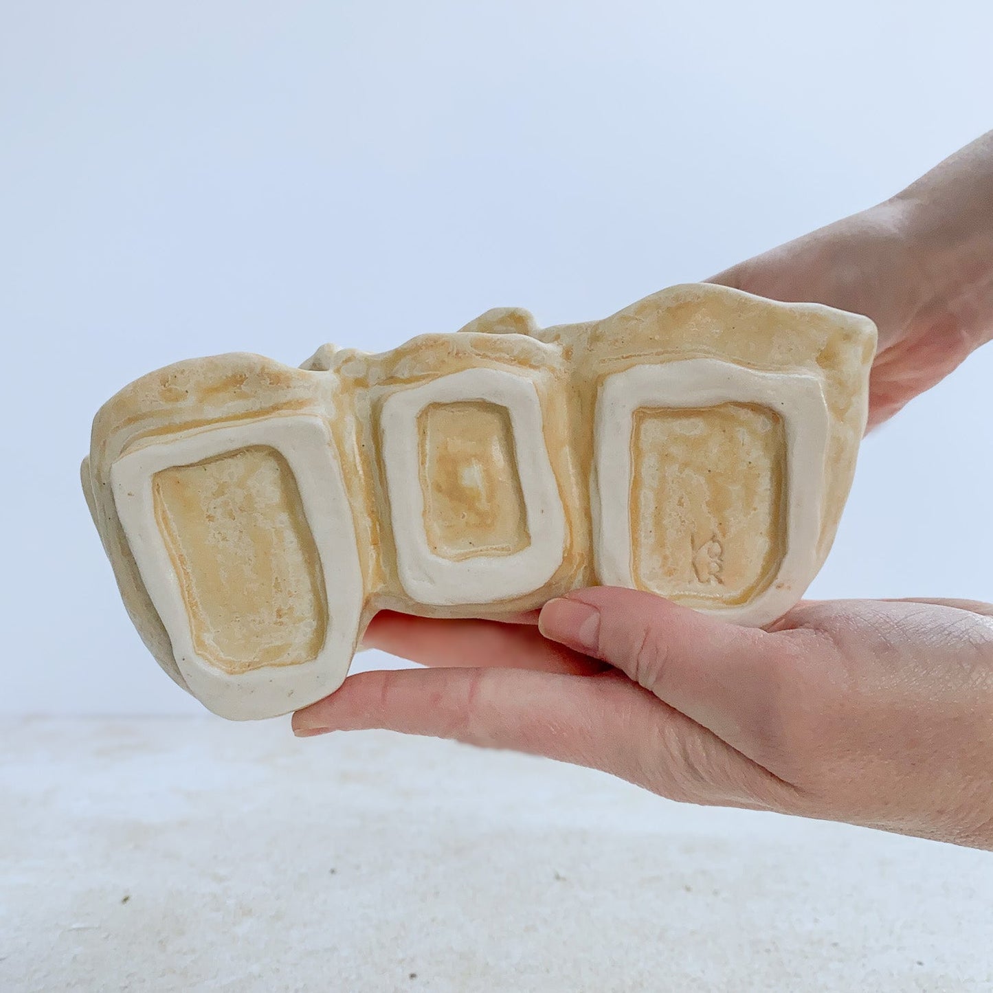 Hands displaying the bottom of a ceramic sculpture on a light background