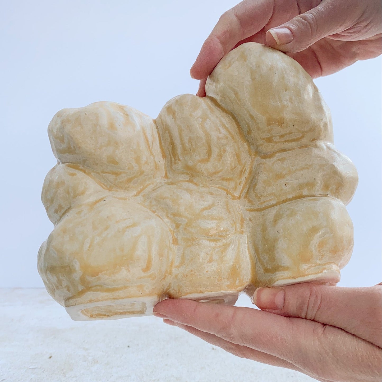 back view of a ceramic sculpture being held by hands on a light background