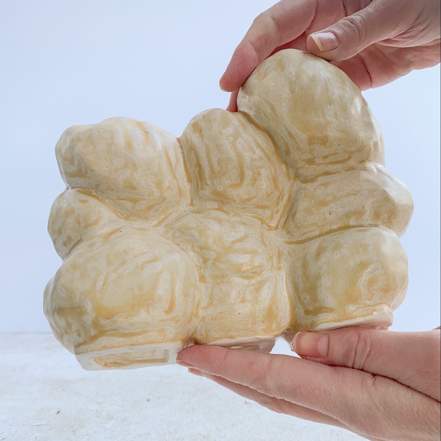 back view of a ceramic sculpture being held by hands on a light background