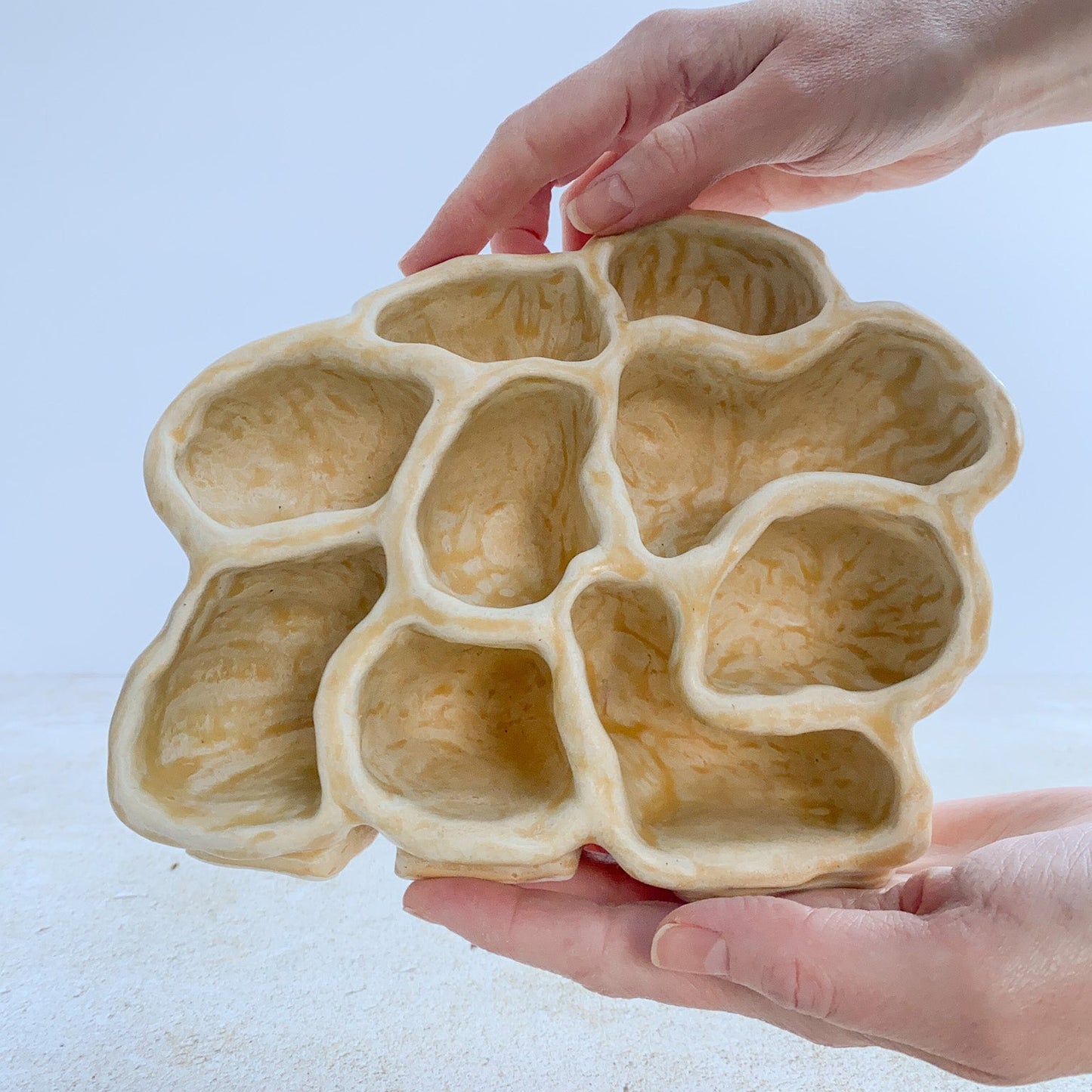 Hands holding a beige ceramic sculpture with a unique design on a light background