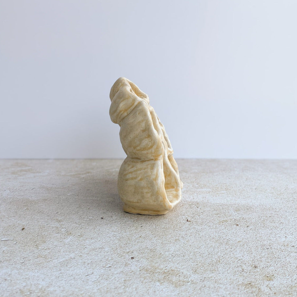 Small beige ceramic sculpture on a textured surface with a light gray background