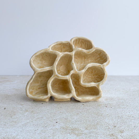 Ceramic sculpture on a grey surface with a white background