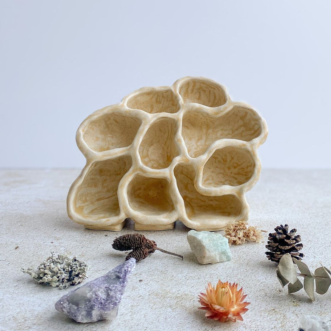 Decorative ceramic sculpture with an organic form on a white surface with small decorative items around it.