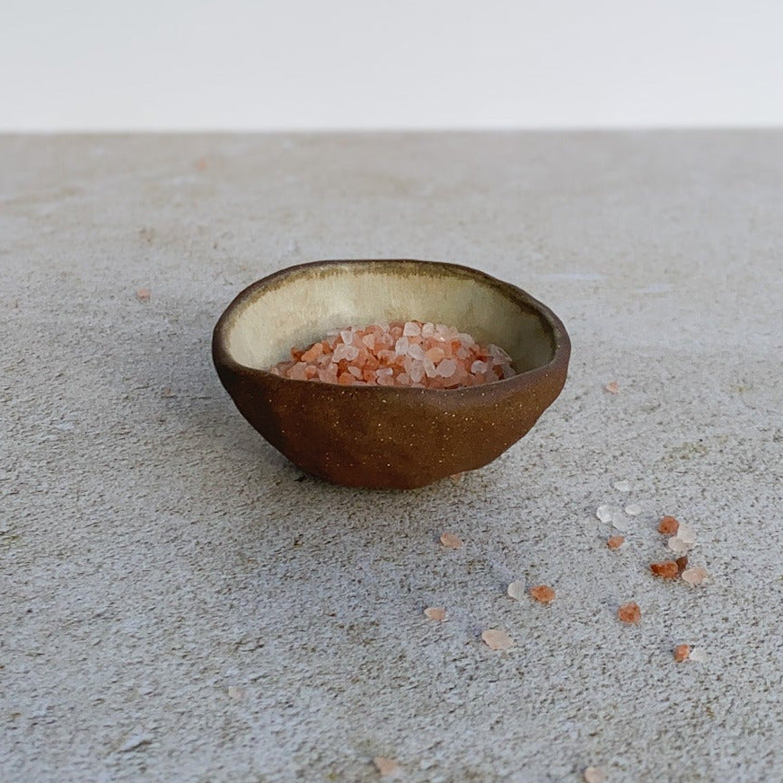 Small brown ceramic bowl on a concrete surface with a white background