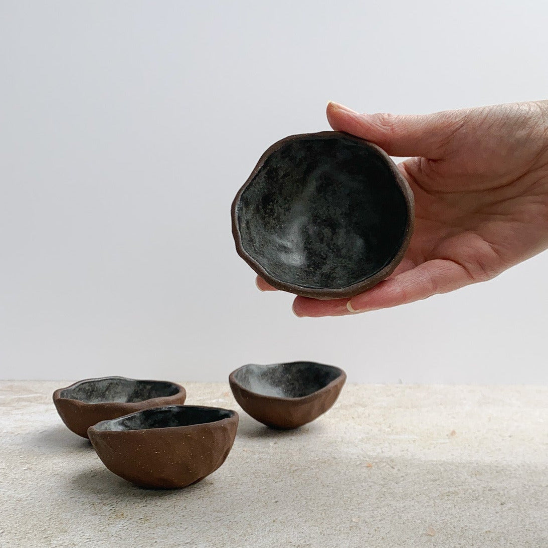 Hand holding a black ceramic bowl with four similar bowls on a light surface.