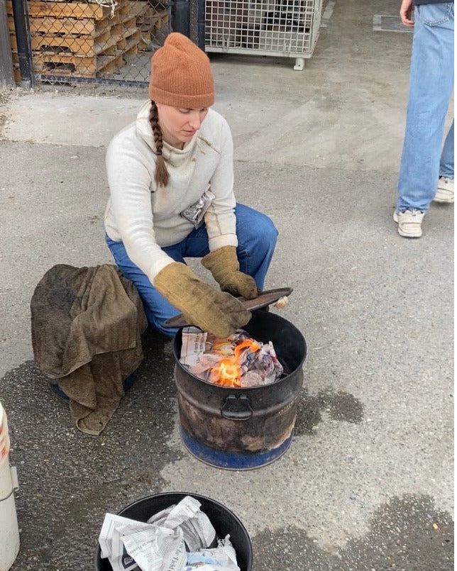 Person putting a lid on a barrel with a fire inside during a raku firing.