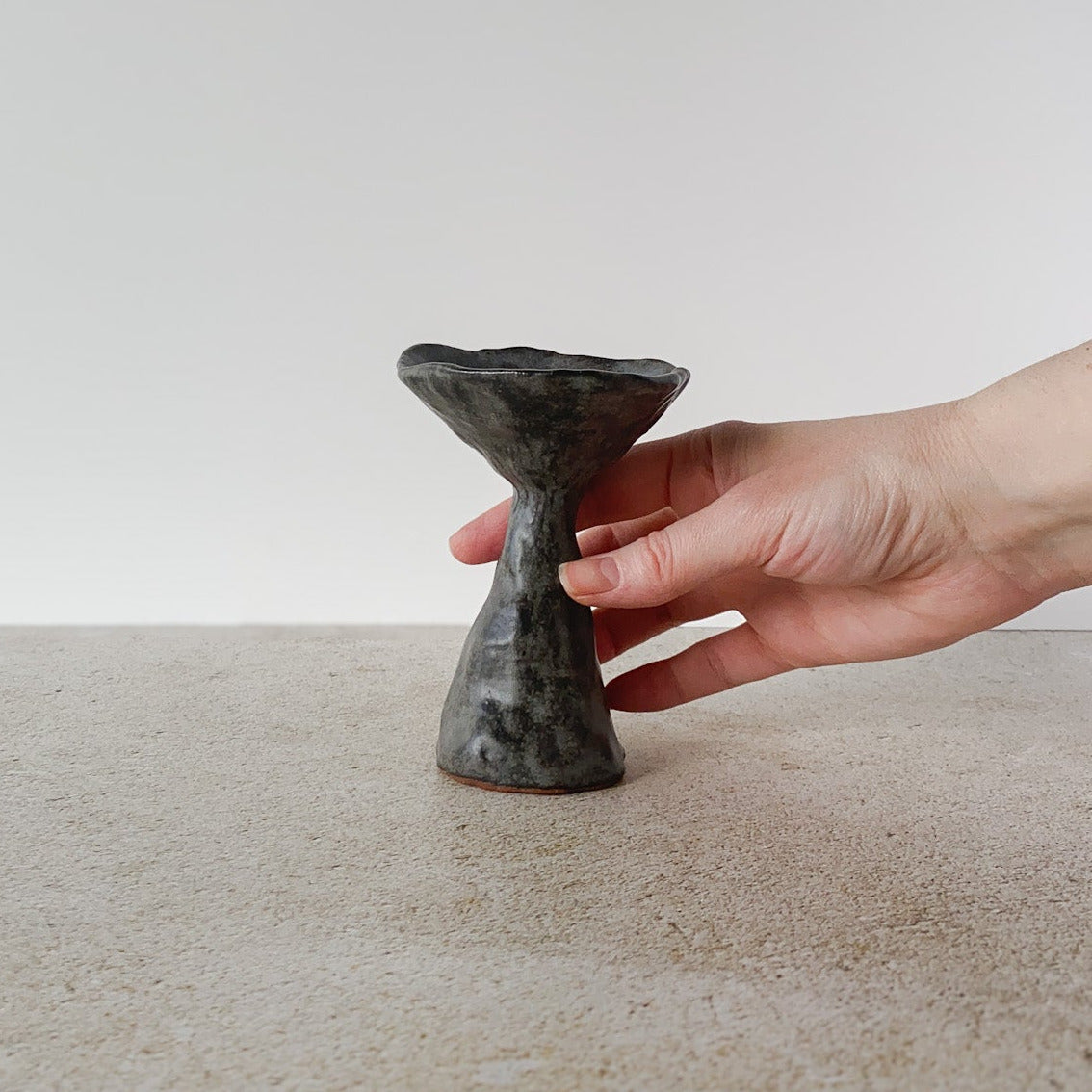Hand holding a small black ceramic mushroom on a light surface with a white background