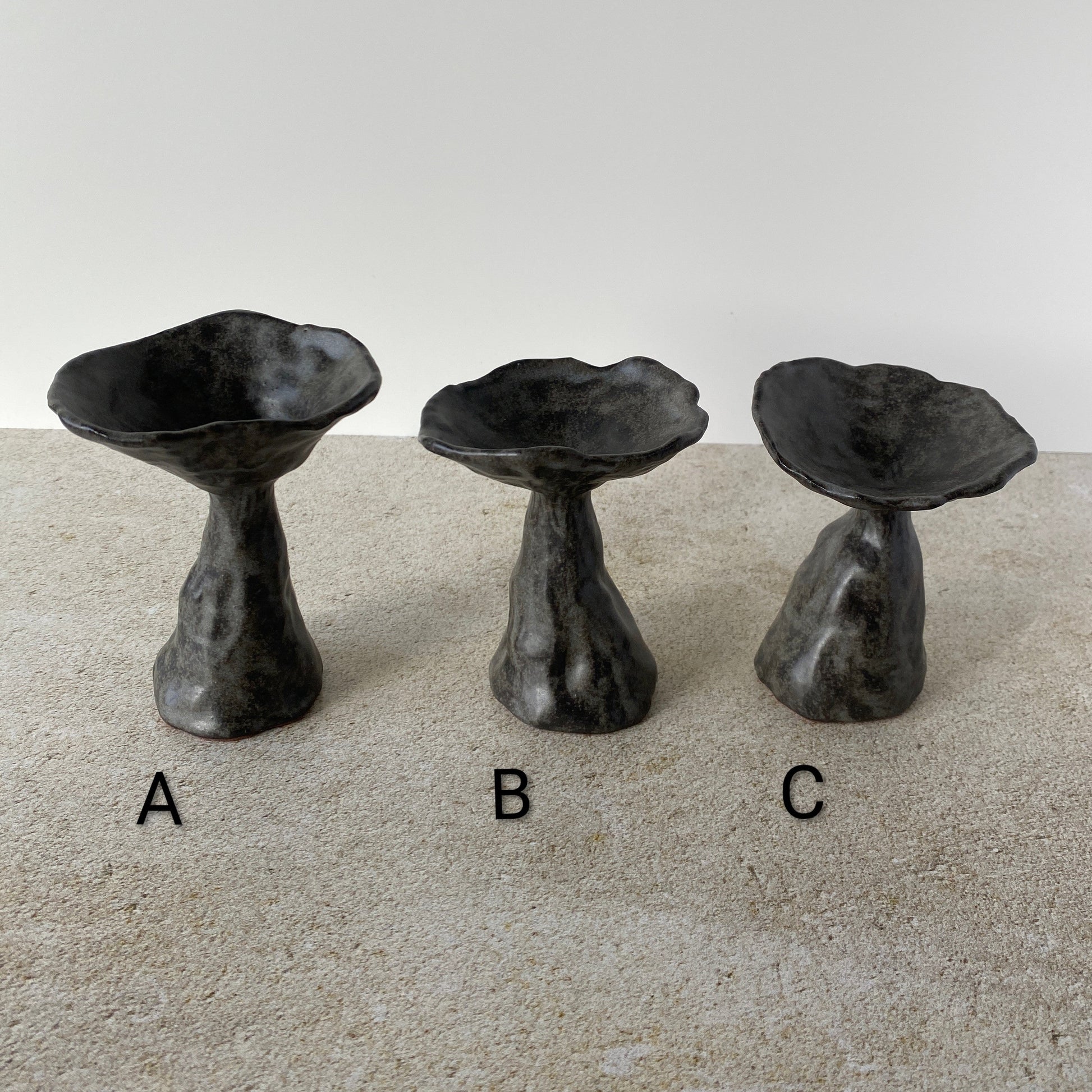 Three black ceramic mushrooms labeled A, B, and C on a beige surface with a white background