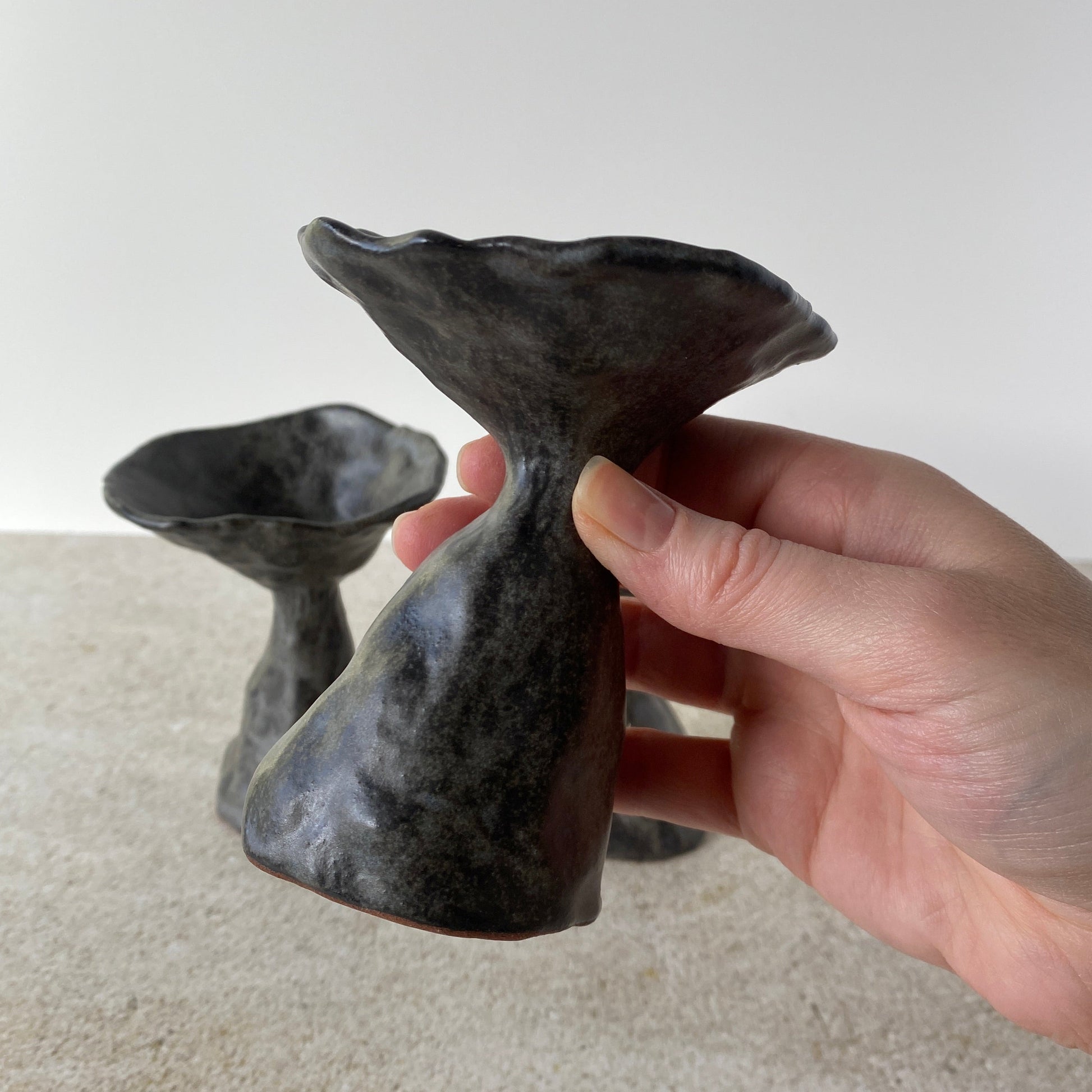 Hand holding a black, abstract ceramic mushroom sculpture against a neutral background
