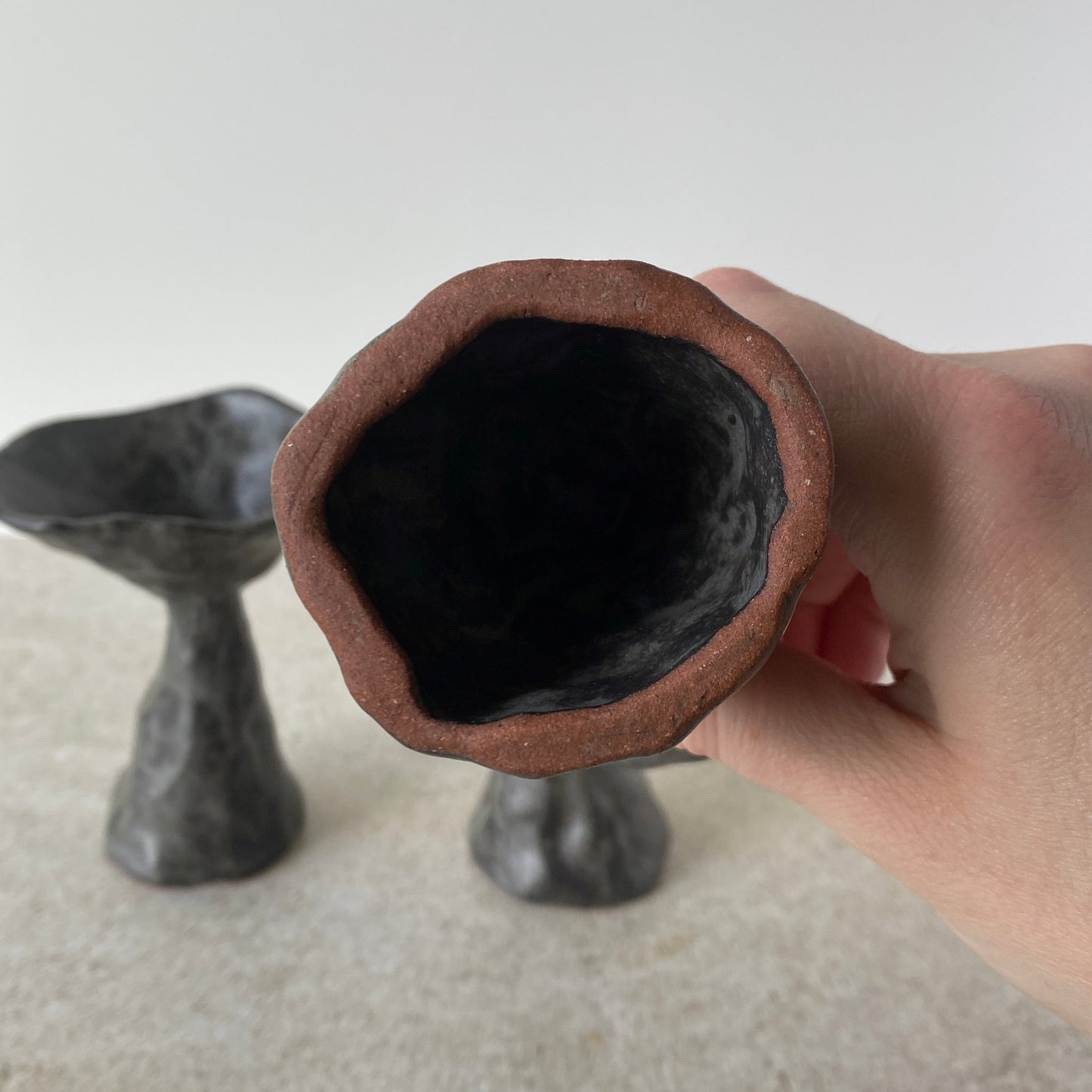 Close-up of a hand holding a cylindrical object with a dark interior against a neutral background