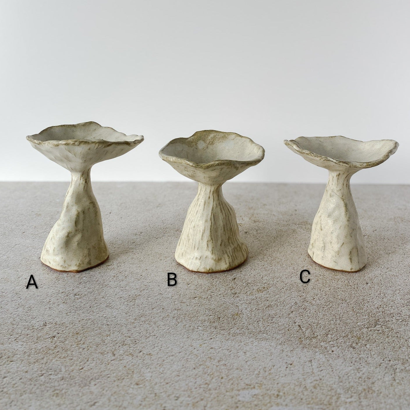 Three ceramic mushrooms of different shapes on a textured surface with a neutral background